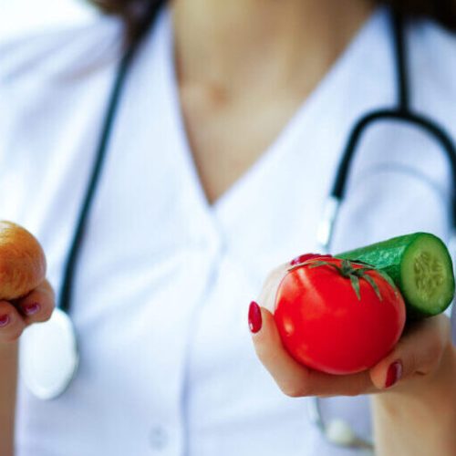 Health and Beauty. The Dietitian Holds Fresh Fruits and Vegetables in the Hands. Young Doctor with a Beautiful Smile. High Resolution.
