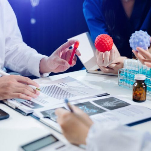 Medical team having a meeting with doctors in white lab coats and surgical scrubs seated at a table discussing a patients working online using computers in the medical industry